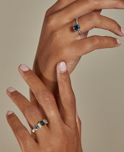 A picture of two hands touching one above the other each with a Sapphire ring on the ring finger centers this frame.